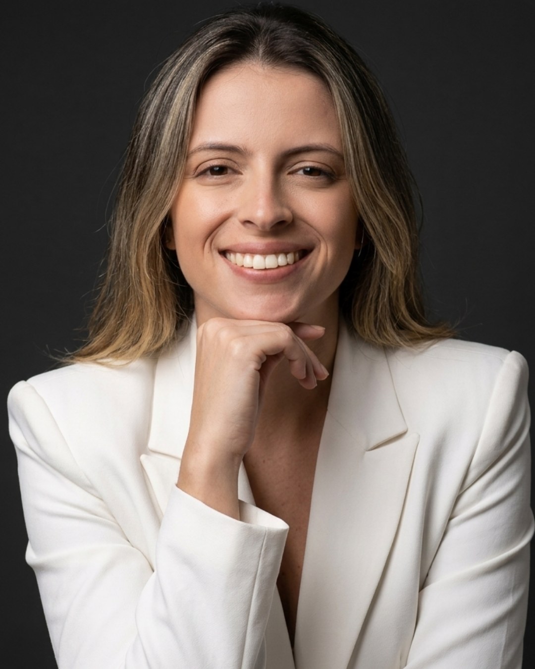 Liliane Corrêa, de blazer branco, sorrindo com o queixo apoiado na mão